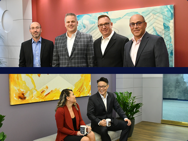 Four professionals in suits pose in a modern office with a blue abstract art piece on a red wall behind them.